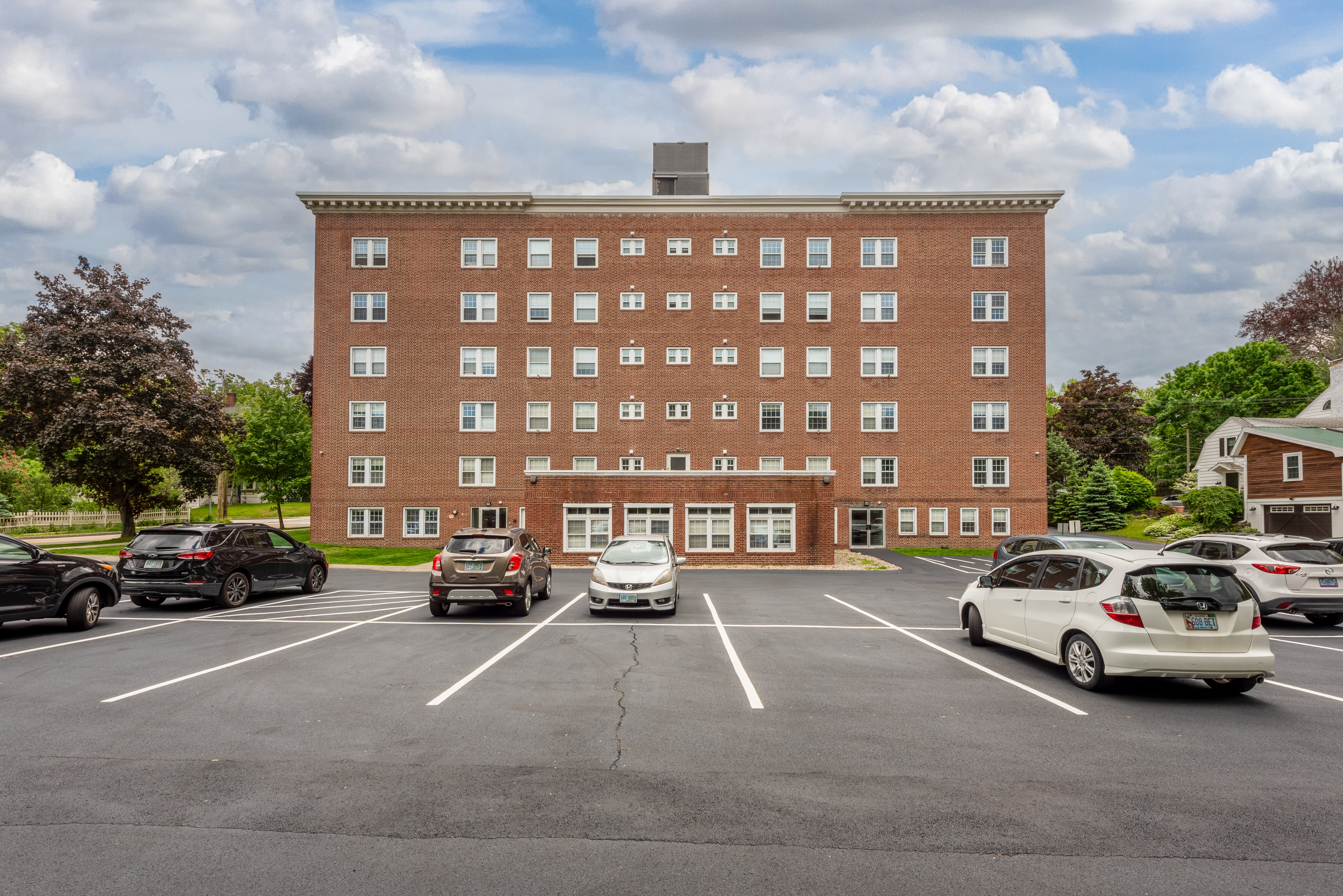 A parking lot in front of a red brick building with cars parked.